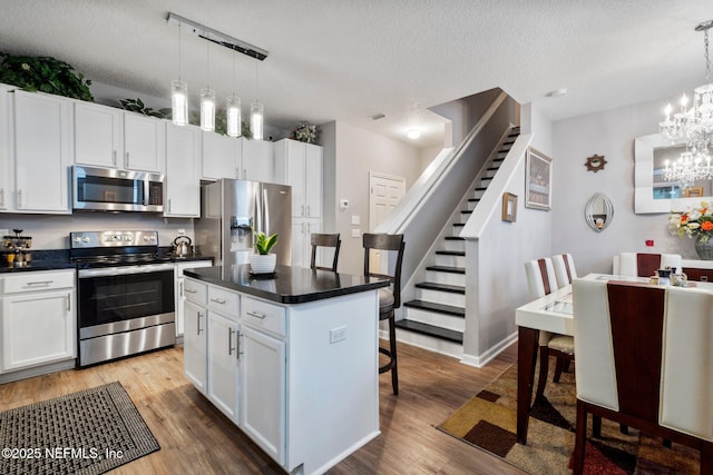 kitchen with a chandelier, stainless steel appliances, dark countertops, and wood finished floors