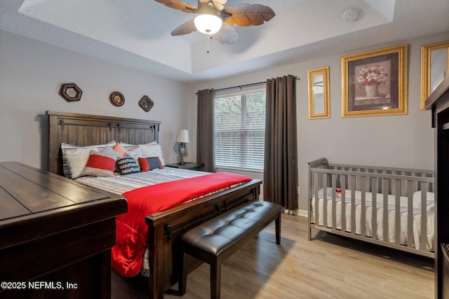 bedroom with ceiling fan, baseboards, a raised ceiling, and wood finished floors