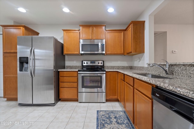 kitchen with brown cabinets, appliances with stainless steel finishes, a sink, and light stone countertops