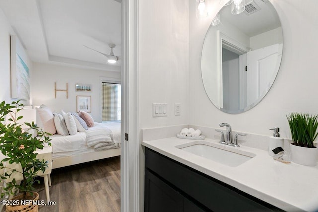 bathroom with wood-type flooring, vanity, ceiling fan, and a tray ceiling