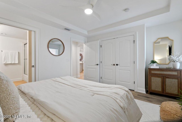 bedroom featuring ensuite bathroom, wood-type flooring, a raised ceiling, a closet, and ceiling fan