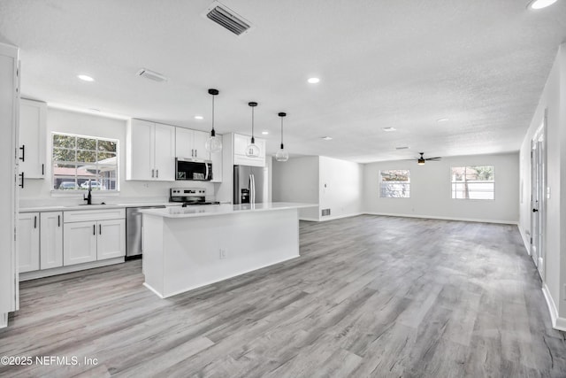 kitchen featuring pendant lighting, a wealth of natural light, white cabinetry, a center island, and stainless steel appliances