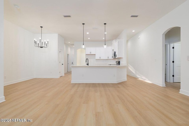 kitchen featuring pendant lighting, sink, a kitchen island with sink, white cabinets, and light wood-type flooring