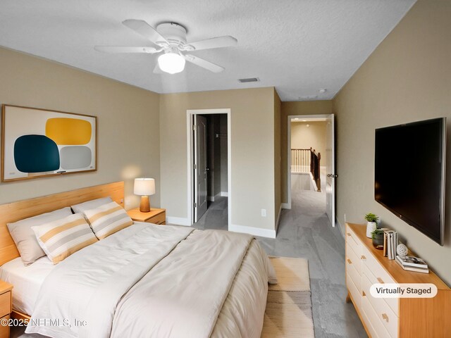 bedroom featuring ceiling fan, ensuite bath, light carpet, and a textured ceiling
