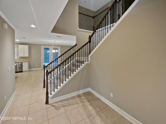 stairs with tile patterned floors, crown molding, and a towering ceiling