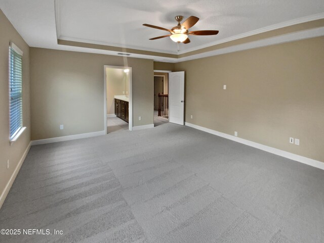 unfurnished bedroom featuring ornamental molding, a raised ceiling, light colored carpet, and ensuite bathroom