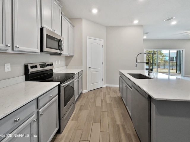 kitchen featuring sink, light stone counters, light wood-type flooring, appliances with stainless steel finishes, and an island with sink