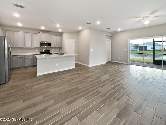 kitchen with sink, gray cabinetry, wood-type flooring, appliances with stainless steel finishes, and a kitchen island with sink