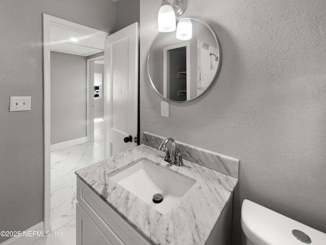 half bathroom featuring marble finish floor, a textured wall, toilet, vanity, and baseboards