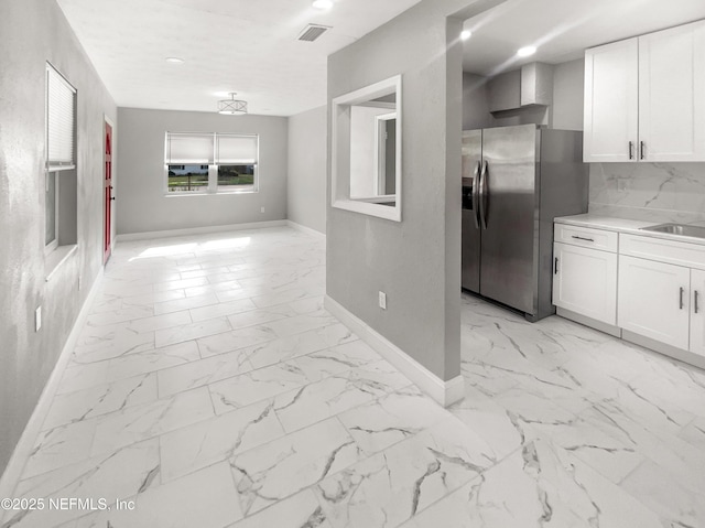 kitchen featuring marble finish floor, light countertops, stainless steel fridge, and white cabinetry