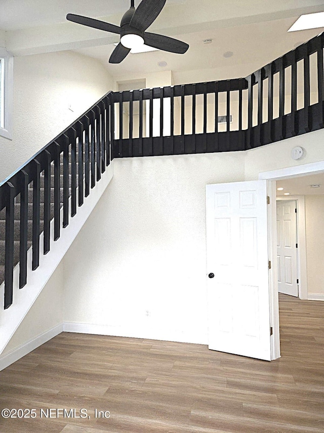 stairway with wood-type flooring, ceiling fan, and a high ceiling