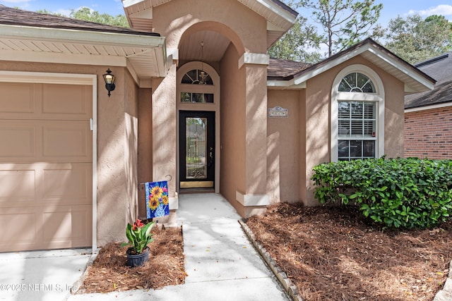 entrance to property featuring a garage, roof with shingles, and stucco siding