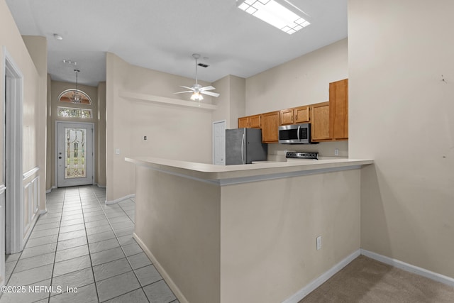 kitchen featuring baseboards, a peninsula, stainless steel appliances, light countertops, and brown cabinets