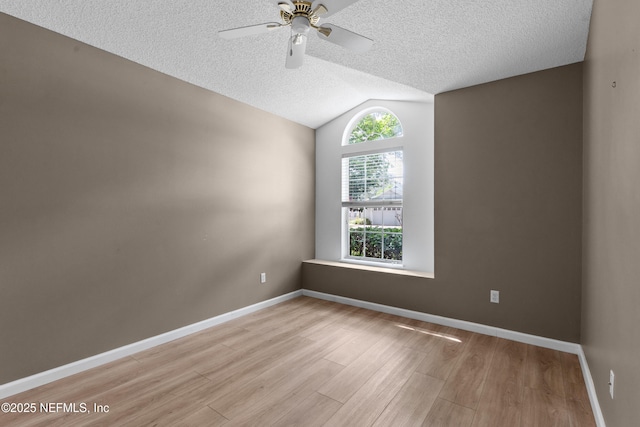 empty room featuring a textured ceiling, wood finished floors, baseboards, and vaulted ceiling