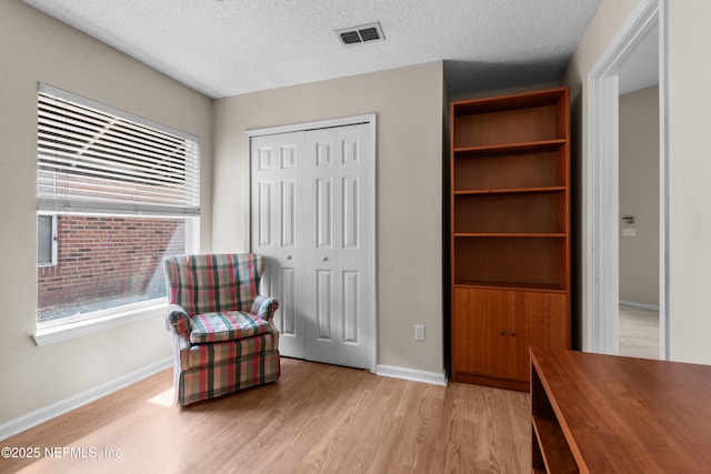 living area featuring visible vents, light wood-style flooring, a textured ceiling, and baseboards