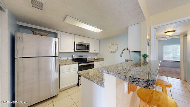 kitchen featuring visible vents, white cabinets, a peninsula, stainless steel appliances, and a kitchen bar