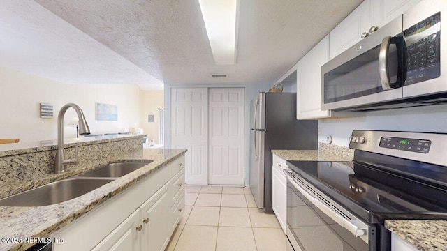 kitchen with visible vents, light stone countertops, stainless steel appliances, white cabinetry, and a sink