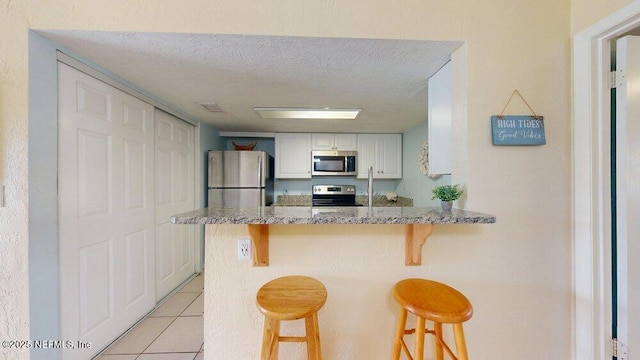 kitchen featuring white cabinets, a kitchen bar, stainless steel appliances, and a peninsula