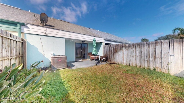 back of property featuring roof with shingles, a patio, a lawn, central AC unit, and a fenced backyard