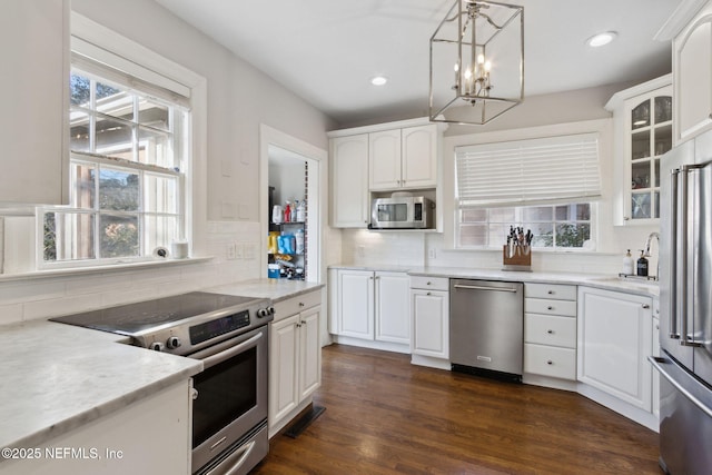 kitchen featuring hanging light fixtures, stainless steel appliances, decorative backsplash, sink, and white cabinetry