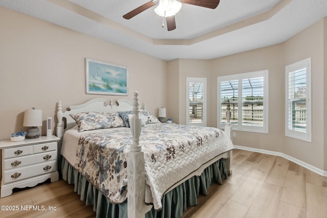 bedroom with ceiling fan, light hardwood / wood-style floors, and a tray ceiling