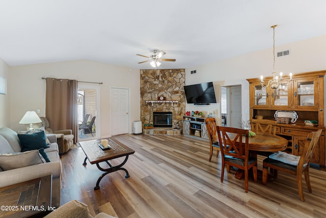 living room with light wood-type flooring, lofted ceiling, a stone fireplace, and ceiling fan with notable chandelier