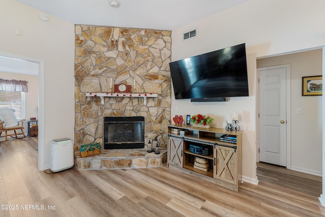 living room featuring light wood-type flooring and a stone fireplace