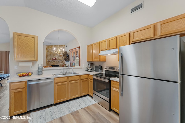 kitchen featuring appliances with stainless steel finishes, decorative light fixtures, light hardwood / wood-style floors, vaulted ceiling, and sink