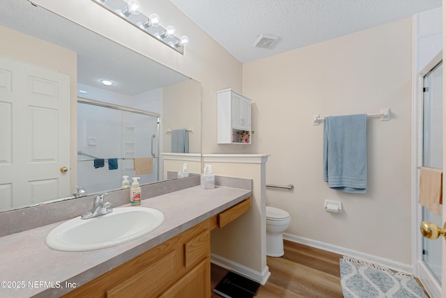 bathroom with hardwood / wood-style floors, a shower with shower door, vanity, a textured ceiling, and toilet