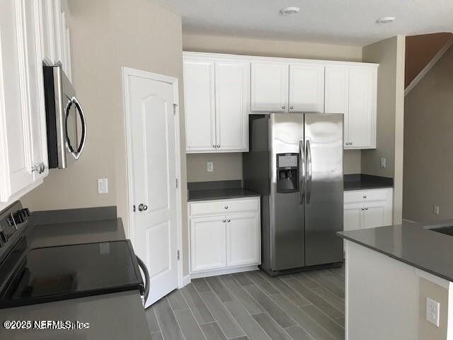 kitchen with dark countertops, wood tiled floor, white cabinetry, and stainless steel appliances