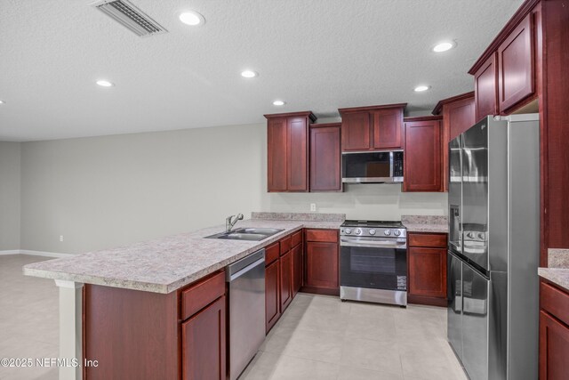 kitchen with visible vents, appliances with stainless steel finishes, a peninsula, dark brown cabinets, and a sink