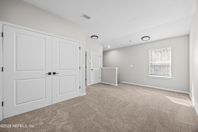 interior space featuring a closet, visible vents, carpet flooring, a textured ceiling, and baseboards