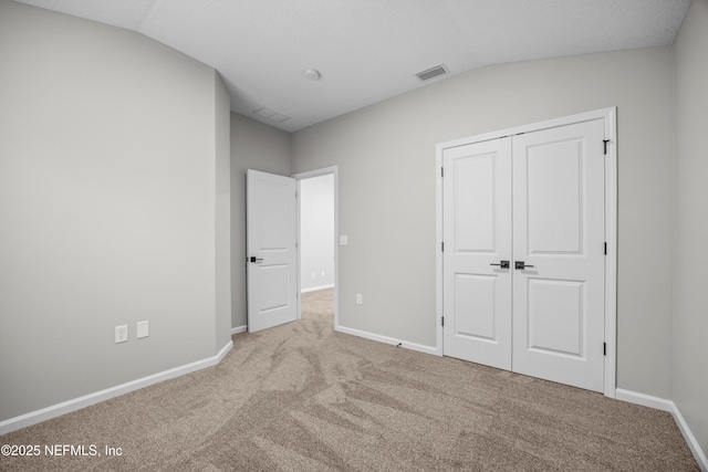 unfurnished bedroom with lofted ceiling, carpet, visible vents, and baseboards