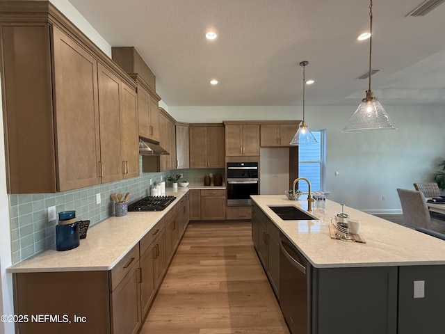 kitchen featuring an island with sink, decorative light fixtures, sink, appliances with stainless steel finishes, and decorative backsplash