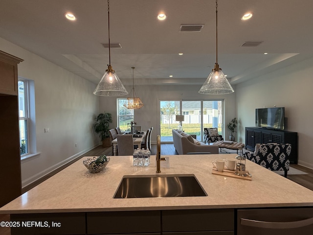 kitchen with stainless steel dishwasher, decorative light fixtures, sink, and a kitchen island with sink