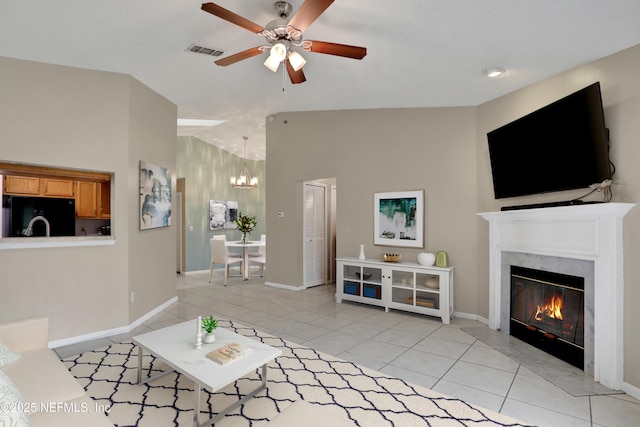 tiled living room featuring ceiling fan with notable chandelier, a high end fireplace, and vaulted ceiling