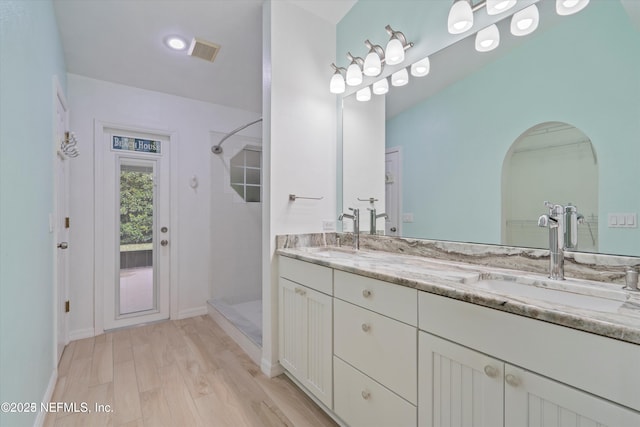 bathroom with a sink, visible vents, tiled shower, and double vanity