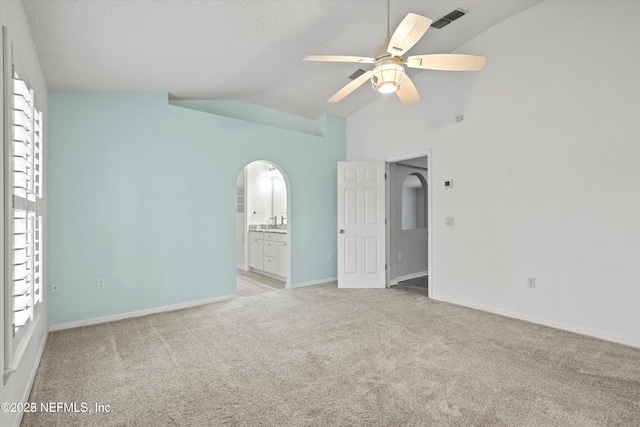 unfurnished room with baseboards, light colored carpet, vaulted ceiling, arched walkways, and a ceiling fan