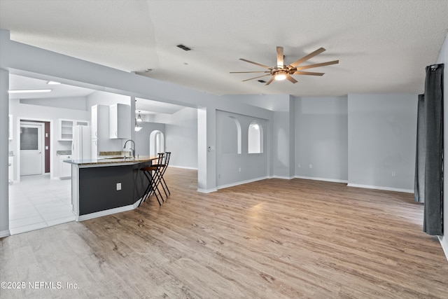 living room with visible vents, baseboards, light wood finished floors, ceiling fan, and a textured ceiling