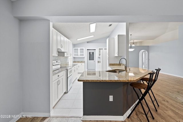 kitchen featuring a breakfast bar, a peninsula, electric stove, arched walkways, and a sink