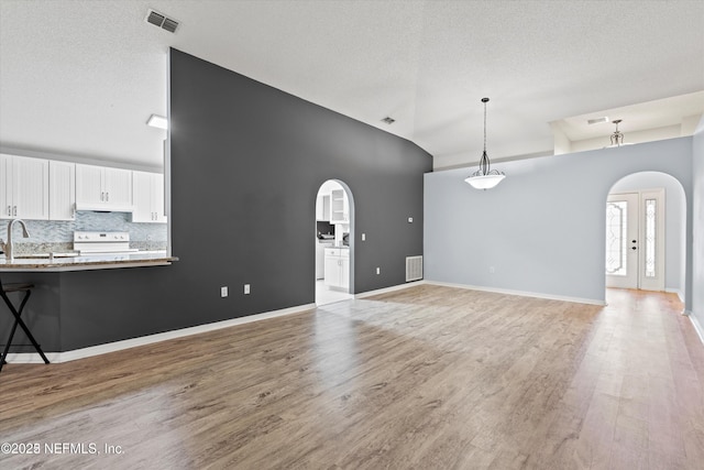 unfurnished living room featuring light wood-style floors, vaulted ceiling, visible vents, and arched walkways