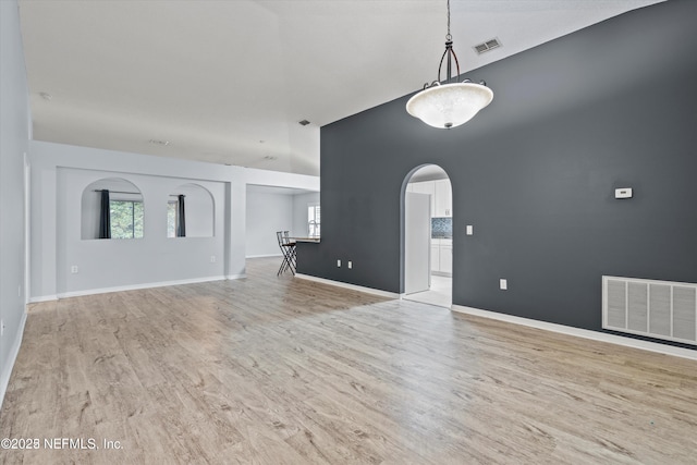 unfurnished living room featuring visible vents, arched walkways, baseboards, and wood finished floors