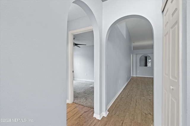 hallway featuring baseboards, arched walkways, and wood finished floors