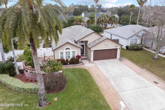 view of front of house featuring a front lawn, fence, stucco siding, a garage, and driveway