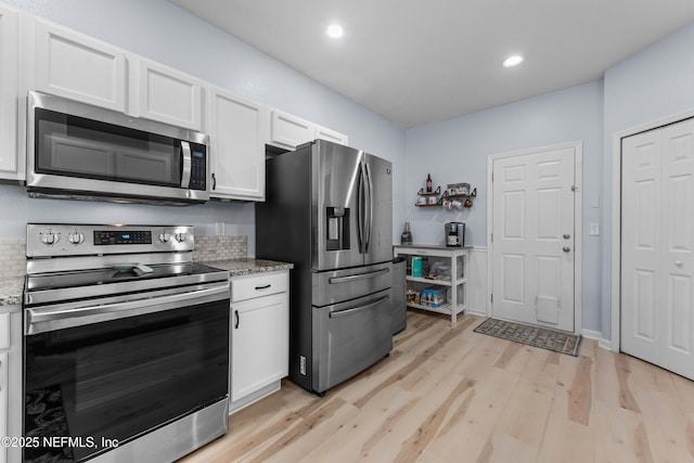 kitchen featuring light hardwood / wood-style floors, appliances with stainless steel finishes, white cabinets, and light stone counters