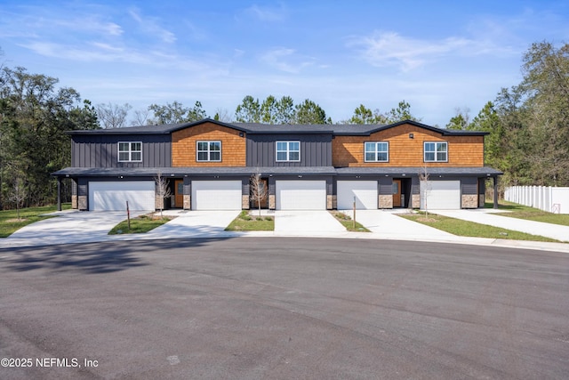 view of front facade featuring a garage, fence, stone siding, driveway, and board and batten siding