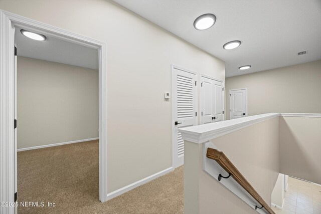 corridor with visible vents, baseboards, an upstairs landing, and light colored carpet