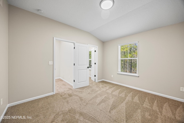 unfurnished room with vaulted ceiling, carpet floors, a textured ceiling, and baseboards