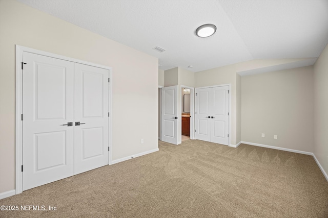 unfurnished bedroom with visible vents, baseboards, carpet, vaulted ceiling, and multiple closets