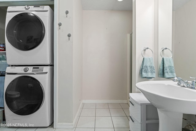 clothes washing area with light tile patterned floors, sink, and stacked washer / dryer